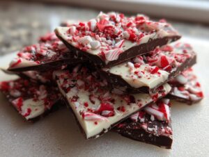 A stack of broken pieces of dark and white chocolate peppermint bark topped with crushed candy canes.