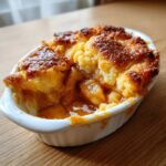 A close-up view of a warm, individual apple cobbler with a golden, crumbly topping and bubbling fruit filling.
