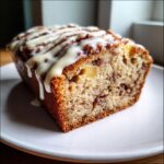 Close-up of a moist slice of apple bread topped with a thick vanilla glaze drizzle.