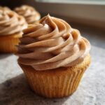 Close-up of a moist banana cupcakes topped with a swirl of light brown, speckled frosting.