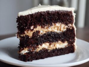 Close-up of a moist slice of chocolate peanut butter cake with three dark layers and creamy peanut butter filling.