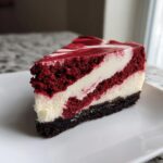 A perfect slice of red velvet cheesecake showing layers of dark red cake and white cream cheese filling.