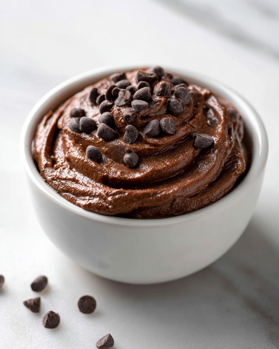Close-up of rich, swirl-textured brownie batter dip topped with chocolate chips in a white bowl.
