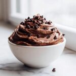 A white bowl filled high with rich, swirled brownie batter dip, generously topped with mini chocolate chips.