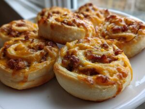 A plate of golden brown sausage pinwheels topped with melted cheddar cheese, ready to eat.
