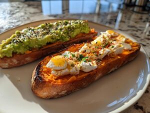 Two slices of sweet potato toast, one topped with avocado and sesame seeds, the other with eggs and cheese.
