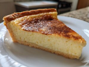 A close-up slice of creamy, baked egg custard tart with a golden, caramelized top dusted with spice.