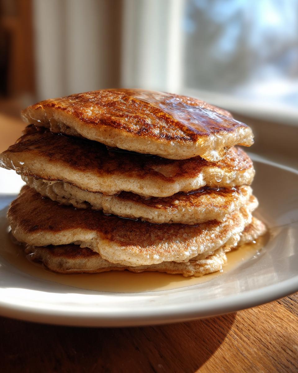 Close-up of a tall stack of fluffy almond flour pancakes drizzled with maple syrup on a white plate.
