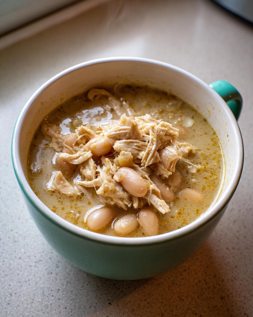 Close-up of a steaming bowl of creamy chicken chili topped with shredded chicken and white beans.