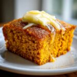 A close-up of a moist slice of sweet potato cornbread topped with melting honey butter.