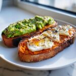 Two slices of vibrant orange sweet potato toast, one topped with mashed avocado and sesame seeds, the other with an egg and honey.