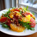 Close-up of a vibrant citrus salad featuring orange and grapefruit slices, arugula, and candied pecans.