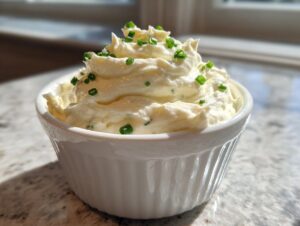 Whipped creamy horseradish sauce, piped high and garnished with fresh green chives, in a white ramekin.