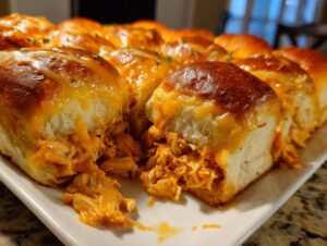 Close-up of freshly baked buffalo chicken sliders with melted cheddar cheese oozing out, served on a white platter.