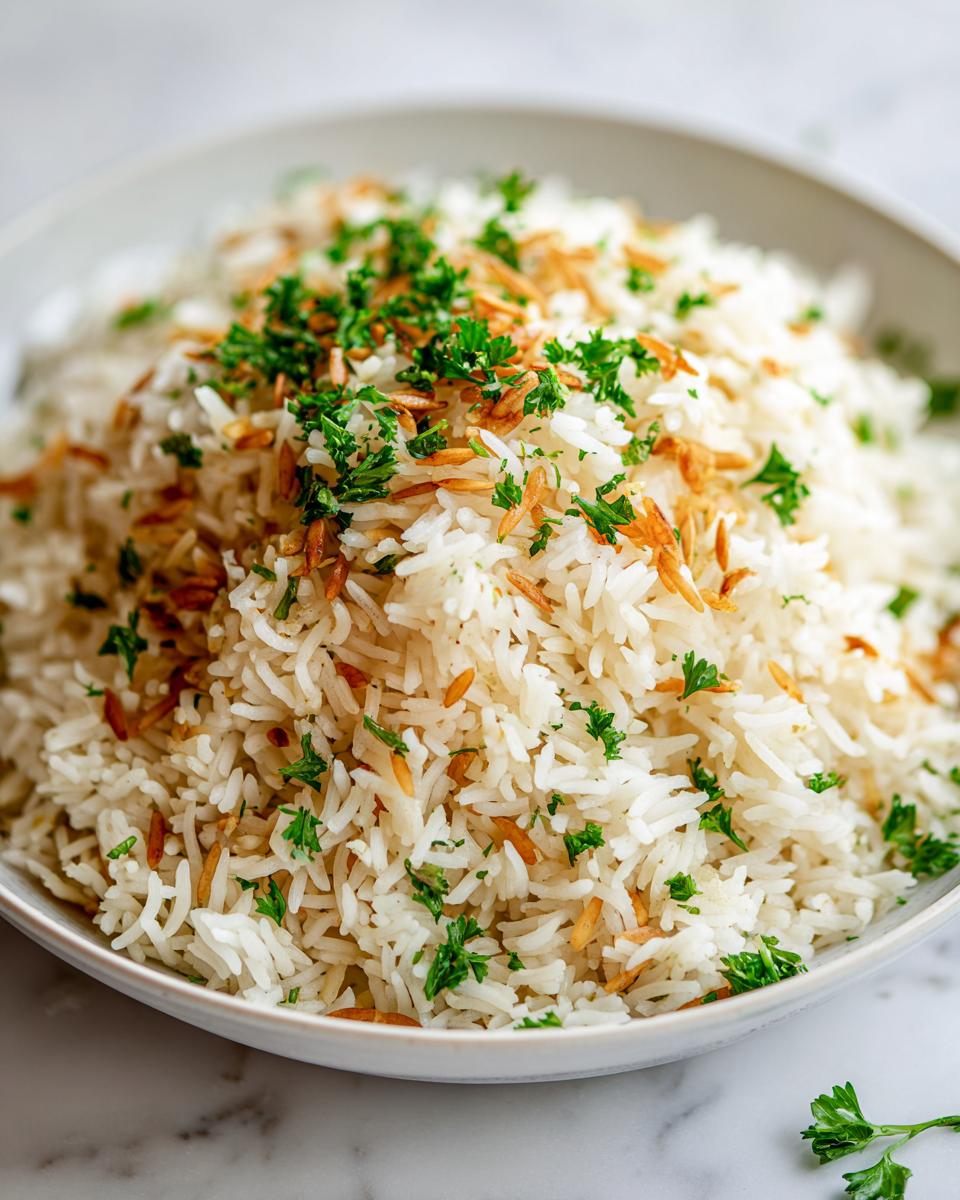 Close-up of fluffy white rice pilaf mixed with toasted vermicelli and topped with fresh chopped parsley.