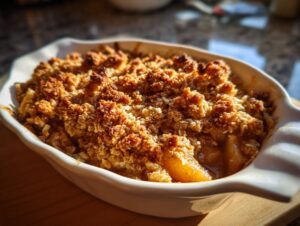 Close-up of a freshly baked apple crisp in a white dish, featuring a golden, crunchy oat topping.