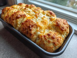 A golden brown loaf of pull-apart cheese bread topped with melted, bubbly cheddar and herbs, fresh from the oven.