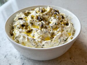A creamy, white olive dip topped with chopped olives, herbs, and a drizzle of olive oil in a white bowl.