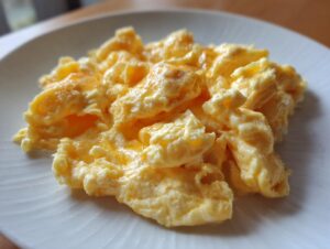 Close-up of perfectly cooked, creamy scrambled eggs piled high on a white plate.
