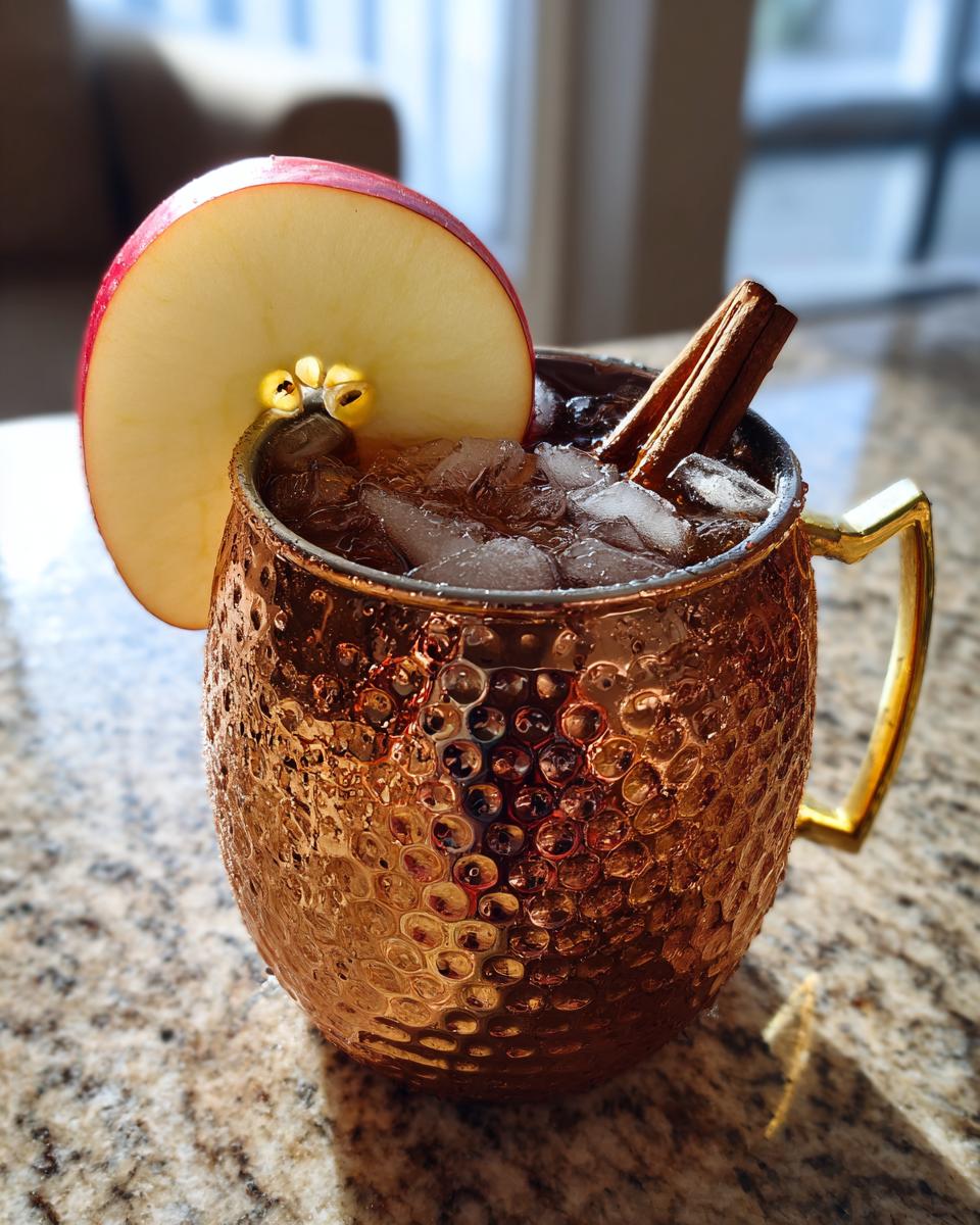 Close-up of an apple cider moscow mule in a hammered copper mug, garnished with an apple slice and cinnamon sticks.