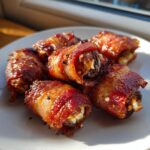 Close-up of several perfectly cooked, bacon-wrapped stuffed dates glistening under sunlight.