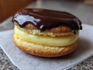 A single, decadent boston cream pie cookie filled with yellow cream and topped with glossy chocolate ganache.