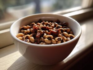 Close-up of cooked black eyed peas mixed with savory pieces of smoked meat in a white bowl.