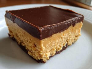 Close-up of a single square of rich buckeye fudge showing a thick peanut butter layer topped with smooth chocolate ganache.