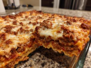 A close-up view of a serving being lifted from a pan of bubbling, cheesy lazy lasagna with rich meat sauce.