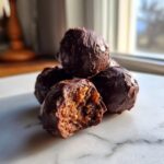 Close-up of chocolate covered pecan pie balls, one with a bite revealing the nutty interior.
