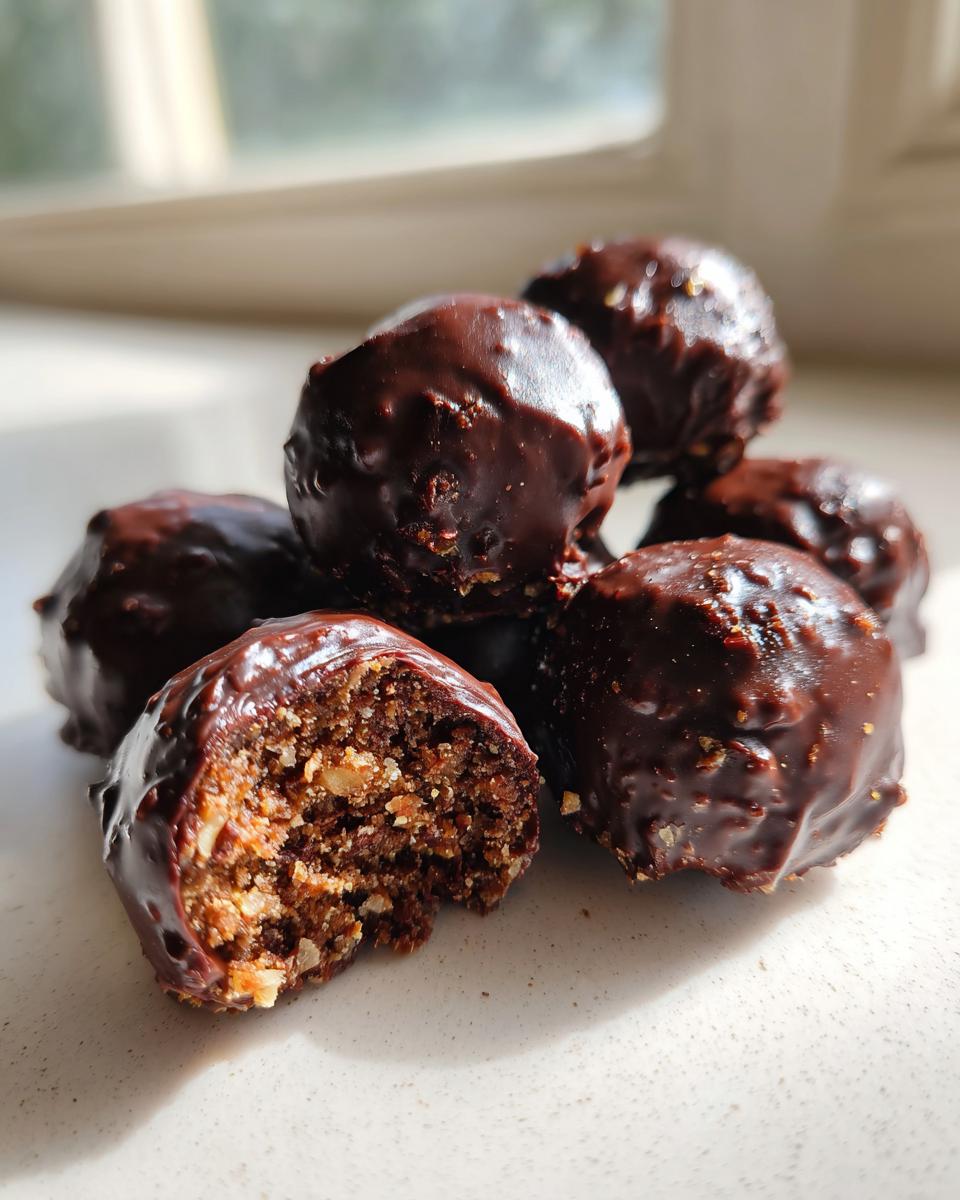 A pile of rich, chocolate-covered pecan pie balls, with one bitten open revealing the nutty interior.
