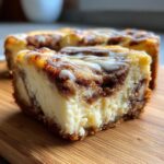 Close-up of a thick slice of cinnamon roll cheesecake showing creamy filling and cinnamon swirl, drizzled with white icing.