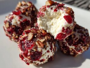 Close-up of several creamy goat cheese balls coated in chopped pecans and dried cranberries, one is broken open.