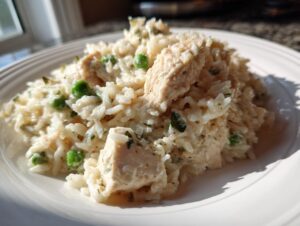Close-up of creamy one pot chicken and rice with green peas served on a white plate.