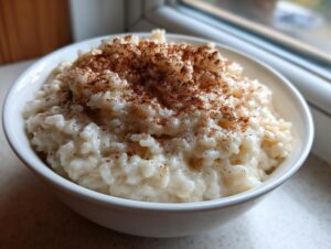 A close-up of a white bowl filled with creamy rice pudding, generously topped with ground cinnamon.