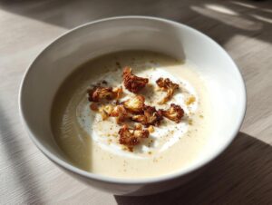 A creamy bowl of roasted cauliflower soup topped with caramelized roasted cauliflower florets and a swirl of cream.
