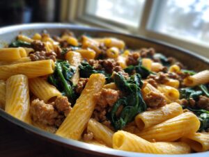 Close-up of creamy sausage pasta mixed with wilted spinach, served in a metal skillet.