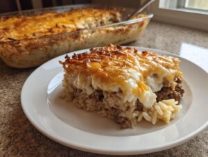 A slice of french onion ground beef and rice casserole with a cheesy, browned top on a white plate.