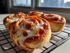 Close-up of four freshly baked pepperoni pizza pinwheels topped with melted cheese, resting on a black wire cooling rack.