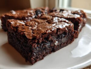 Close-up of a fudgy oreo brownie slice showing a shiny, crackled top and visible white filling.