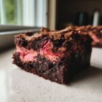 Close-up of a fudgy square of strawberry brownies showing a rich chocolate base and a bright pink, fruity strawberry swirl center.