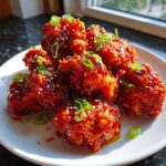 Close-up of crispy Korean fried chicken pieces coated in a thick, glossy red sauce, garnished with sesame seeds and scallions.