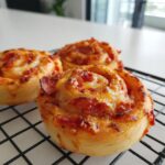 Close-up of three freshly baked pizza pinwheels with melted cheese and pepperoni cooling on a black wire rack.