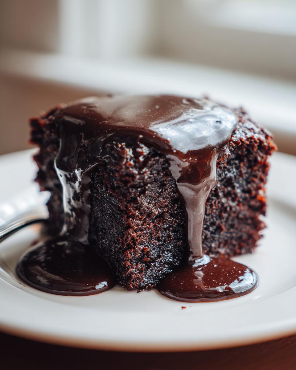 Close-up of a moist slice of chocolate pudding cake drenched in rich, glossy chocolate sauce.