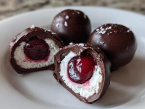 Close-up of homemade chocolate covered cherries, one cut open showing the cherry center and white filling.