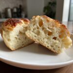 Close-up of homemade English muffins split open, showing the characteristic open, airy crumb structure.