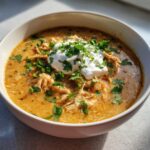 A close-up of a bowl of creamy keto white chicken chili topped with sour cream and fresh cilantro.