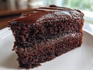 Close-up of a rich, dark slice of chocolate fudge cake topped with thick, glossy chocolate frosting.