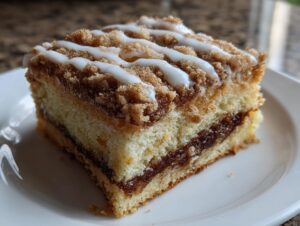 Close-up of a moist slice of coffee cake featuring a cinnamon swirl layer and a sweet vanilla glaze drizzle.