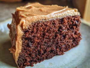 Close-up of a moist slice of dark gingerbread cake topped with thick, creamy brown frosting.